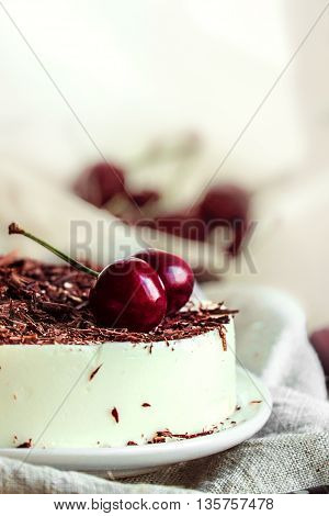 No-bake vanilla bavarian mousse cake with cherries and dark chocolate. Made with cream cheese and whipped cream. White plate and light background.