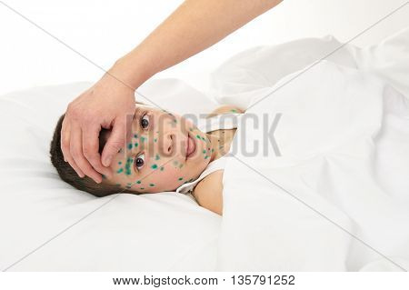 sick child in bed has the virus chickenpox on skin, mother's hand touches the forehead