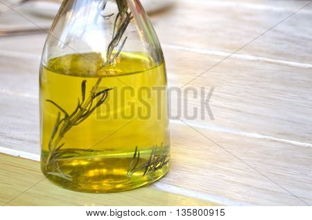 Bottle of olive oil and a sprig of rosemary inside. Transparent glass bottle on a wooden surface. Bottle with vegetable oil. Herb-Infused olive oil.