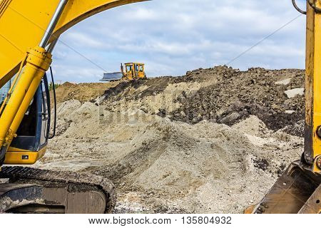 Earth mover is moving earth outdoors leveling ground. View under the arm of excavator.