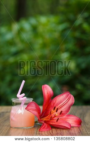 jar of cold pink cocktail with straw on green background bokeh