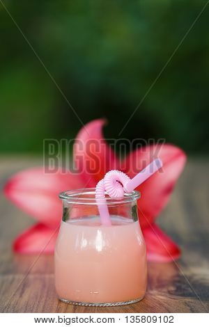 jar of cold pink cocktail with straw on green background bokeh