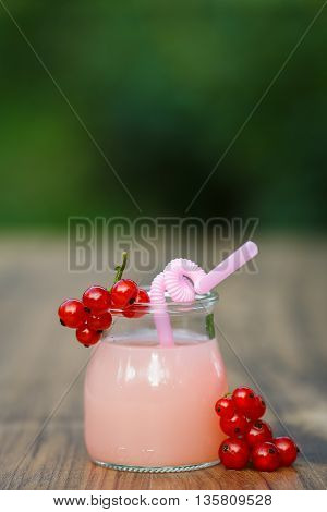 jar of cold pink cocktail with straw on green background bokeh