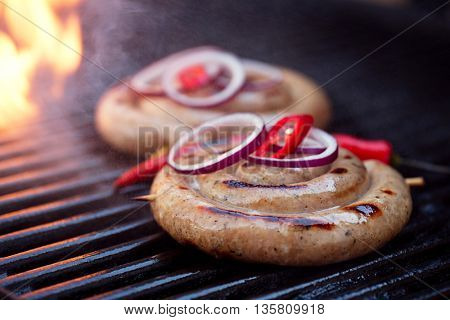 cumberland sausage, spiral pork sausage on bbq grill with flame, homemade