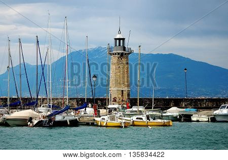 Sirmione Italy - June 1 2006: Stone lighthouse surrounded by moored boats stands on the harbour walls at Lake Garda