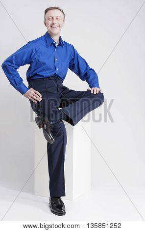Full Length Portrait of Smiling Caucasian Man Sitting on White Box and Laughing. Posing Against White. Vertical Image Orientation