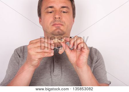 Middle aged man changing a hearing aid battery. Focused on the hand and the hearing aid.