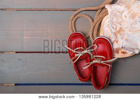 Red boat shoes near big shell and rope on wooden background. Top view/. Copy space. Frame.