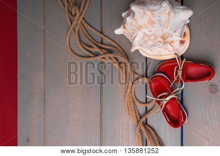 Red boat shoes near big shell and rope on wooden background. Top view/. Copy space. Frame.