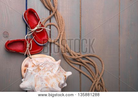 Red boat shoes near big shell and rope on wooden background. Top view/. Copy space. Frame.