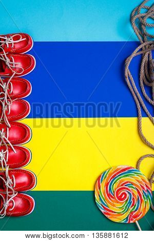 A lot of small red boat shoes near big multi-colored lollipop on colored background. Top view copy space. Frame. group of child boat shoes.