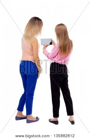 Back view two young woman look at smart phone. Rear view people collection.  backside view of person. Rear view. Isolated over white background. Two blonde girls looking at something in the tablet PC.