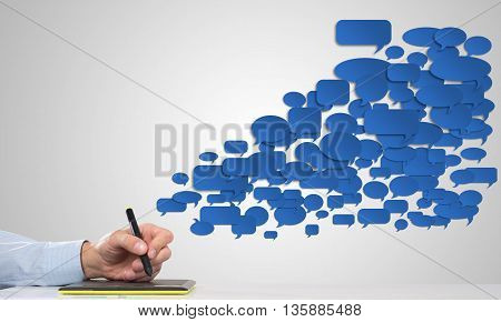 Hand of man using tablet and chatboxes flying out