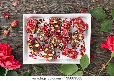 A white rectangular plate full of traditonal turkish delight with rose petals decorated with rose flowers. Dark wooden background, top view.