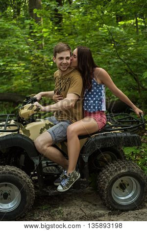 Young couple hugs kisses and smiles on forest road while driving a quad bike on a summer day. Young man and woman on an ATV