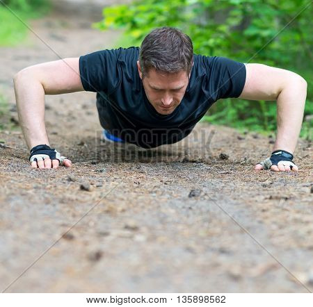 Handsome man doing push-ups in the forest.