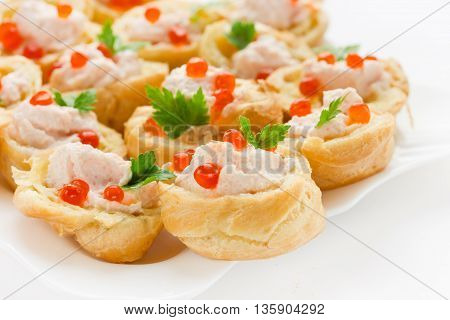 Cocktail snack with red caviar. Tartlets of choux dough with salmon mousse and red caviar on a white plate close up selective focus