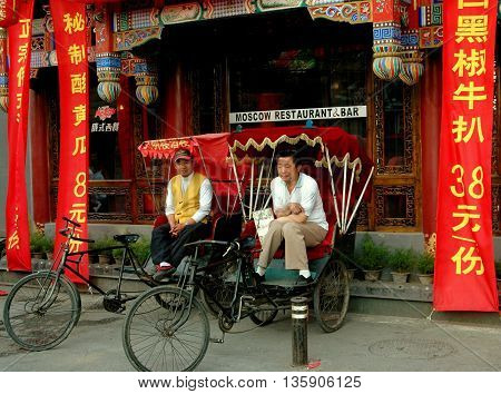 Beijing China - May 5 2005: Two pedicab drivers in their taxis waiting for fares in front of a restaurant & bar at the Shi Sa Hai Hutong