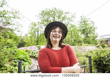 mature brunette fat woman in green garden wearing hat, smiling, friendly welkoming, lifestyle people concept close up