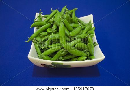 Fresh green peas in white dish on a blue background