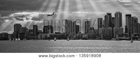 TORONTO SKYLINE IN BLACK AND WHITE WITH SUNBEAMS PROTRUDING THROUGH CLOUDS AND AIRPLANE IN THE DISTANCE