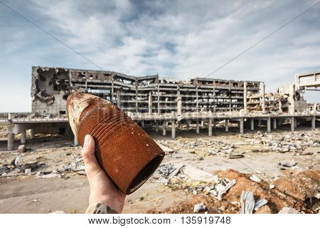 Unexploded 120 mm artillery shell in hand with destroyed Donetsk airport ruins on background