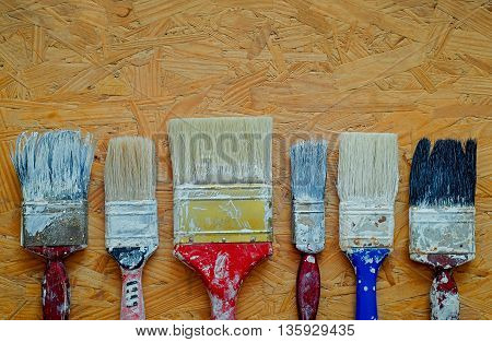 Old paint brushes on pressed wooden panel background