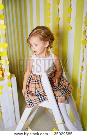 Beautiful little girl sitting on step ladder.Blue-eyed blonde.Children's room. Happy small girl portrait.
