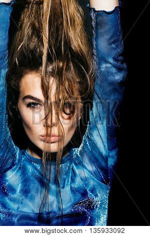Attractive young coguar girl holding wet long hair with hands in blue cloth on dark background