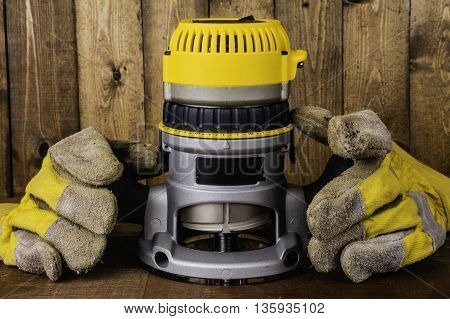 hand held electric fixed base router on wood background with leather work gloves