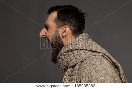 Unleashing his emotions. Side view of furious young bearded man shouting while standing against grey background