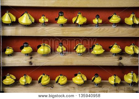wooden cabinet displaying yellow metal router bits on red background