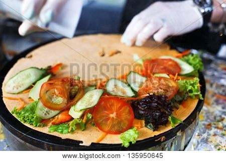 Making vegetable crepe at pan. Salty crepe or pancake with fillings made by street vendor's hands at outdoors creperie. French cuisine, cooking for commercial kitchen.