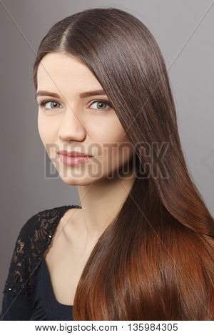 Portrait of young woman demonstrating her long brownhair in studio. Beautiful lady with modern hairstyle over grey background.