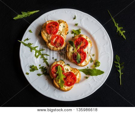 Toasts (Crostini) with ricotta cherry tomatoes and arugula on black background.