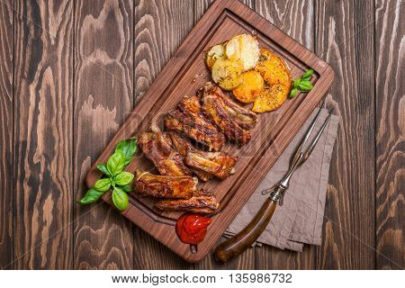 elicious Grilled Pork Rib and Fried Potato Wedges with Sauce on wooden cutting board, top view