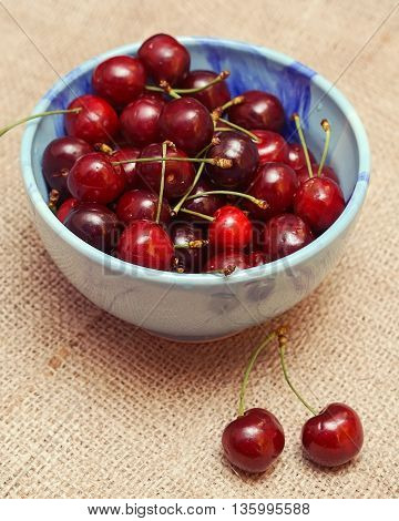 Fresh cherries berries in blue bowl on sackcloth background