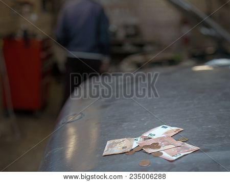 Cash Laid On A Car Hood, A Solhouette Of A Man In The Blurred Background