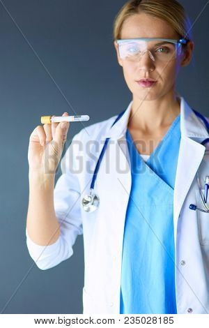 Female medical or research scientist or doctor using looking at a test tube of clear solution in a lab or laboratory.