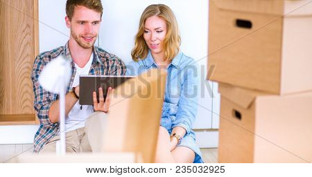 Young couple moving in new home.Sitting and relaxing after unpacking.Looking something on laptop. Young couple