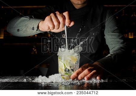 Professional Bartender Prepare A Fresh Lime Cocktail In The Glass With An Ice At The Steel Barstand