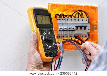 Electrician Technician Working On A Residential Electrical Panel, Measures The Voltage On The Termin