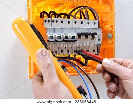 Electrician Technician Working On A Residential Electrical Panel, Measures The Voltage On The Termin
