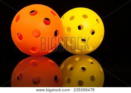 Mirrored Pickleballs.  Orange & Yellow Pickleballs On A Black Background With Mirror Reflection.