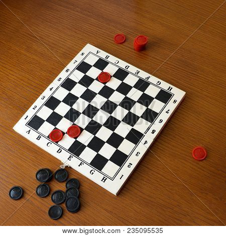 Black And Red Checkers On A Game Board On A Wooden Background