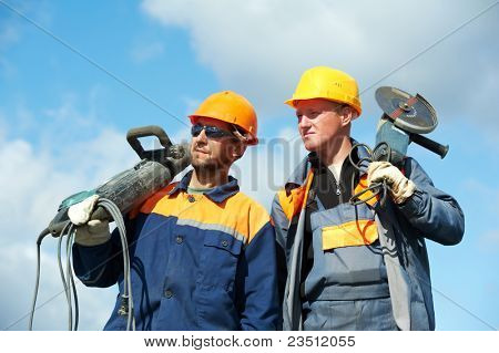 Due operai Builder con martello pneumatico e apparecchiatura della macchina rettificatrice sopra cielo blu