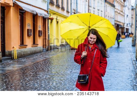 Smiling Woman In Red Coat With Yellow Umbrella Walk By City Street