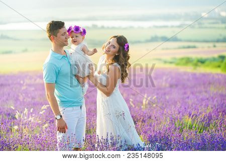 Mom, Dad And Their Little Daughter In A Beautiful Wreath Are Walking In A Lavender Field. Life In Pr