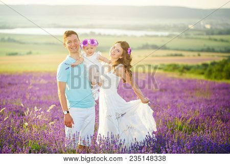 Mom, Dad And Their Little Daughter In A Beautiful Wreath Are Walking In A Lavender Field. Life In Pr