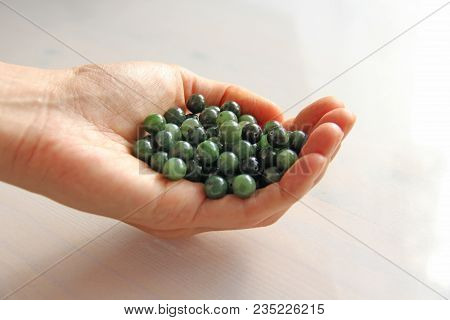 Natural Green Jade Nephrite Mineral Stones Beads. The Green Jade Stone Lies In The Hands. Hands Hold
